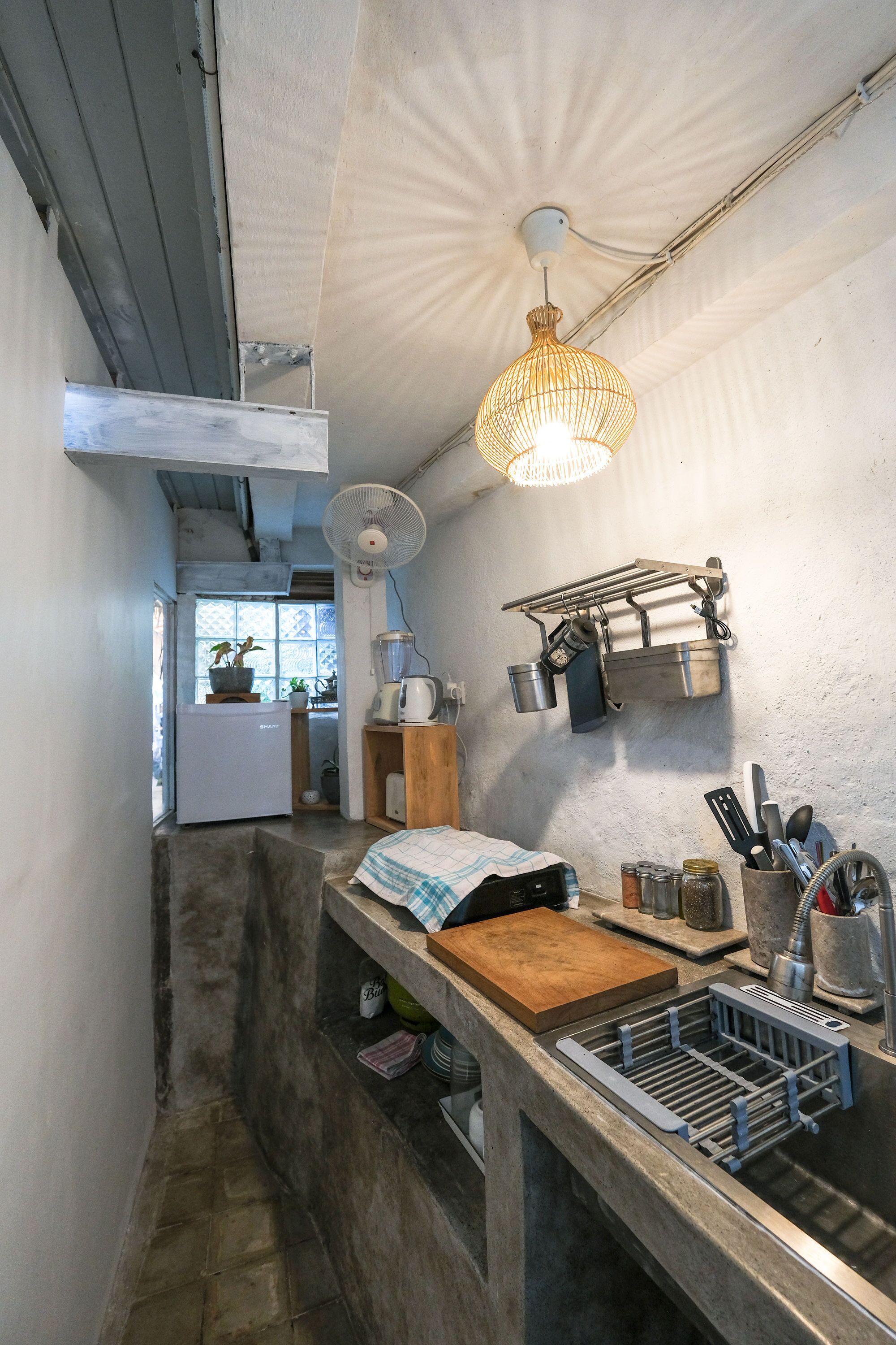 Cocina compacta con lavamanos empotrado, tabla de cortar de madera, colgador de ollas y ventilador de techo.