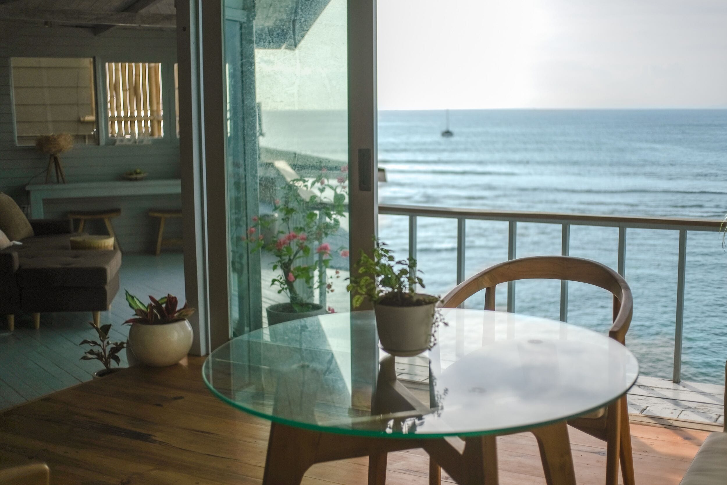 Una mesa de vidrio con sillas sobre una terraza de madera, con vistas al mar.