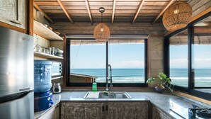 A kitchen with a large window overlooking the ocean, a stainless steel refrigerator, and a wooden ceiling. - Le Cliff Bali (Pecatu)