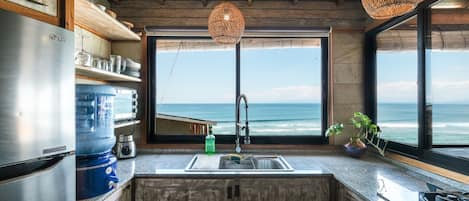 A kitchen with a large window overlooking the ocean, a stainless steel refrigerator, and a wooden ceiling.
