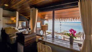 A room with a wooden ceiling, a wooden desk with a lamp, a chair, a bed with pillows, and a window with a view of the sea. - Le Cliff Bali (Pecatu)