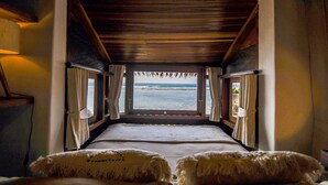 A room with a bed facing a window with curtains, a wooden ceiling, and a view of the sea. - Le Cliff Bali (Pecatu)