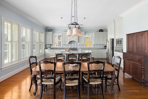 A spacious kitchen with a central island, white cabinetry, and a dining area with wooden chairs. - Upscale Retreat w/ Ocean Views + Pet Friendly (Folly Beach)