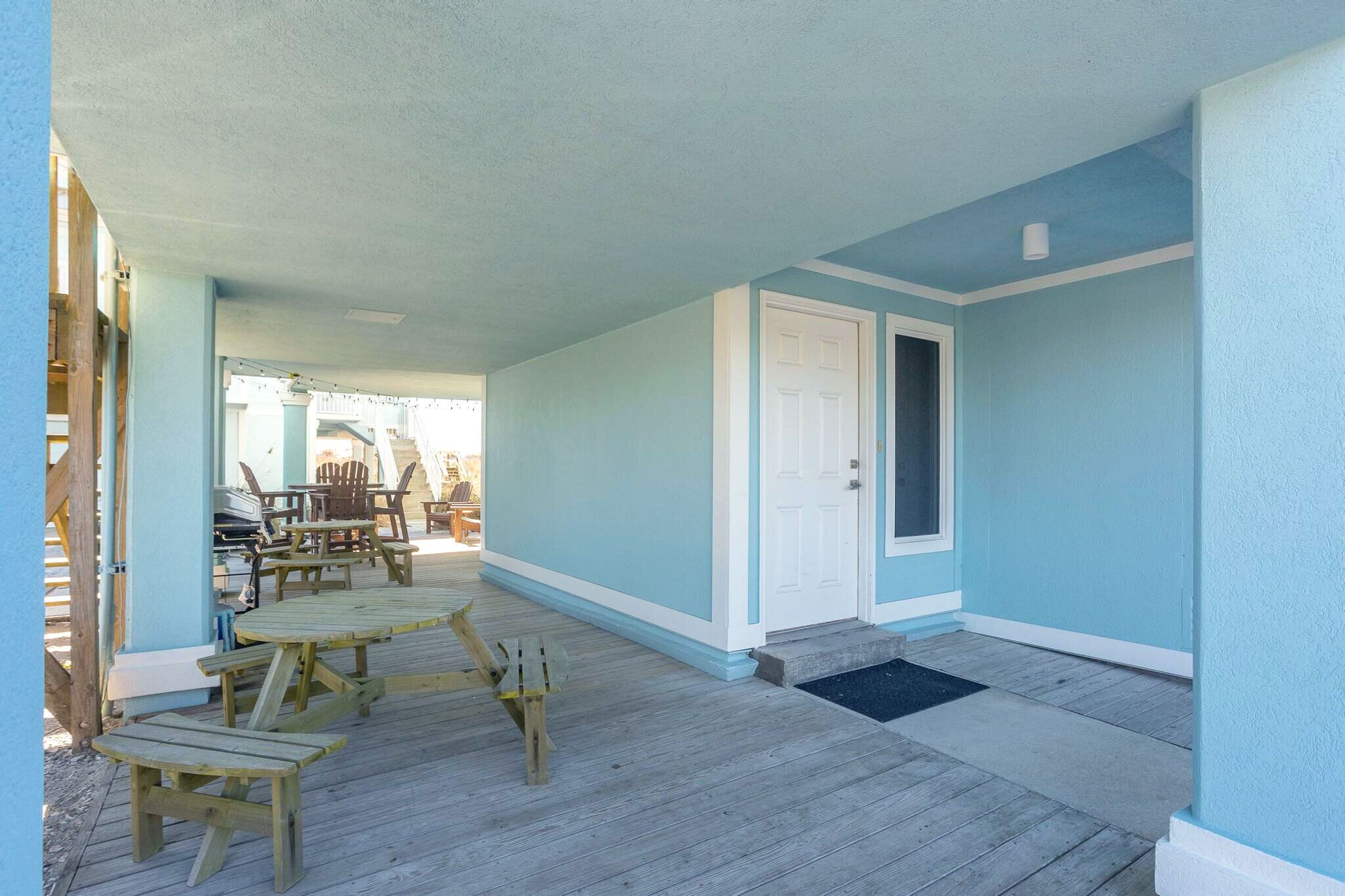 A covered porch with wooden furniture, a door, and a view of the beach.