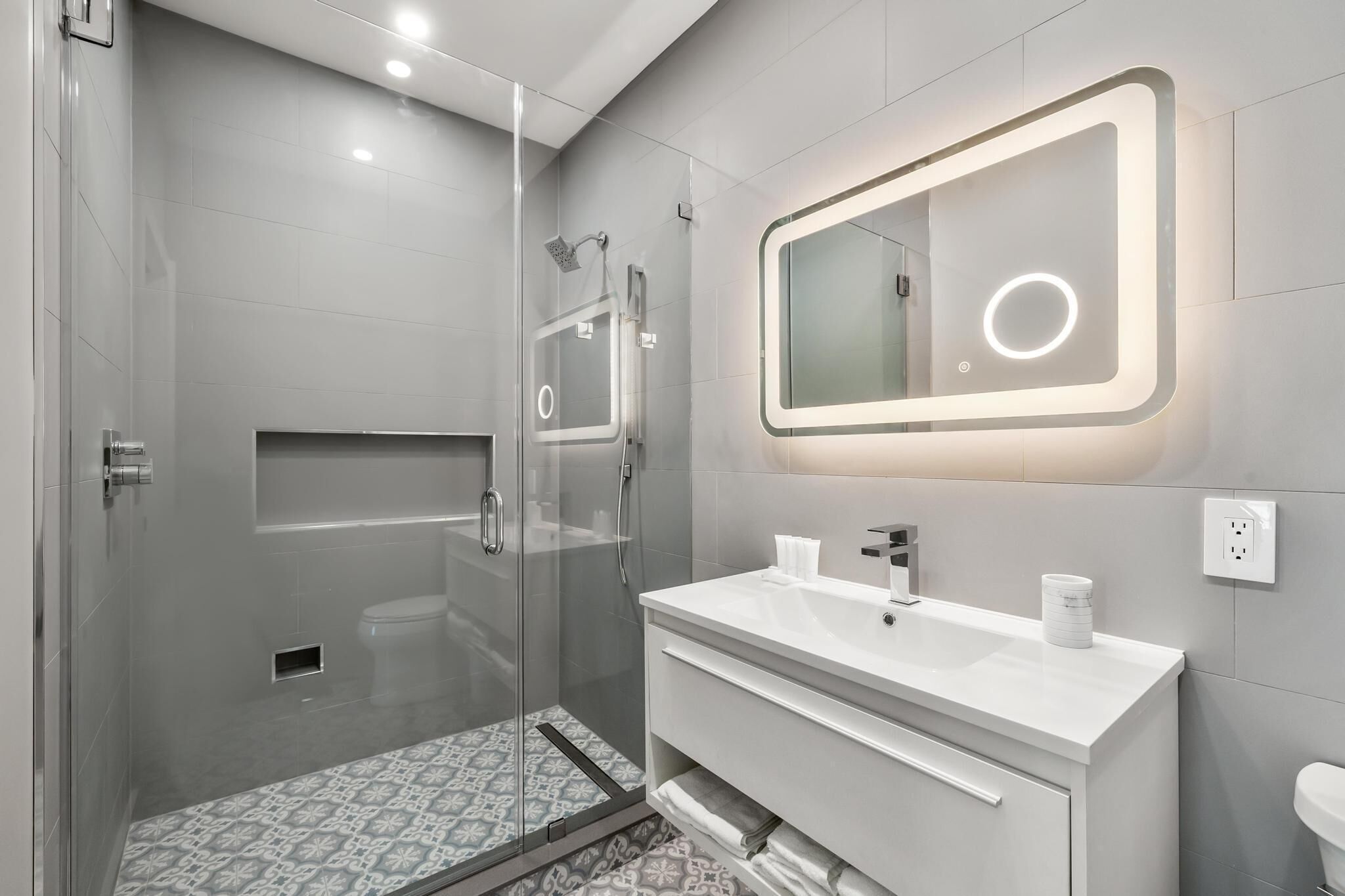 A modern bathroom with a glass-enclosed shower, a white vanity with a mirror, and a patterned shower floor.