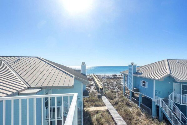 A coastal property with a wooden deck leading to a beach, featuring a clear view of the ocean.