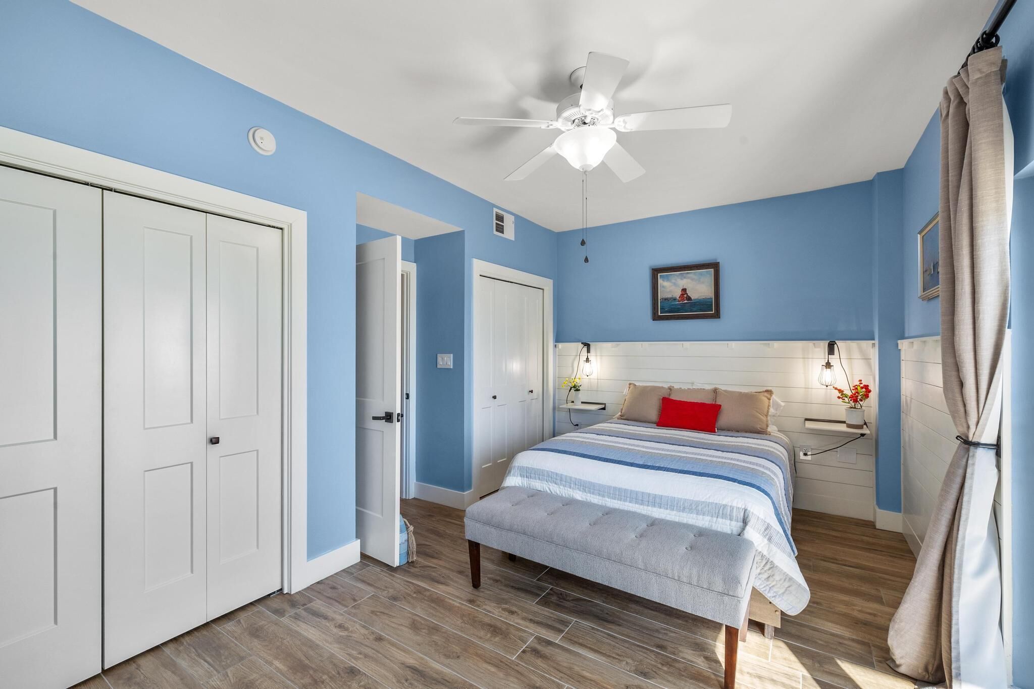 Une chambre à coucher avec un lit, des tables de chevet, un ventilateur de plafond et une porte.