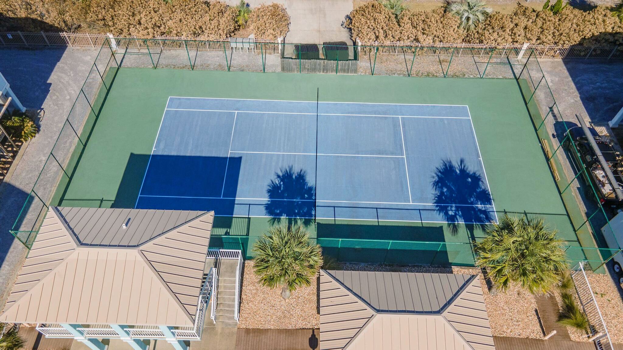 Vista aérea de una cancha de tenis con jardines y una edificación.