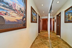 A hotel hallway with tiled flooring, wooden doors, and framed artwork on the walls. - Beautiful updated 2bd condo, a sleek new finish (Lahaina)