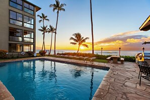 A swimming pool with a sunset view, palm trees, and a building with large windows.