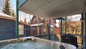Un bain à remous sur une véranda, avec vue sur une maison rouge et un garage bleu.