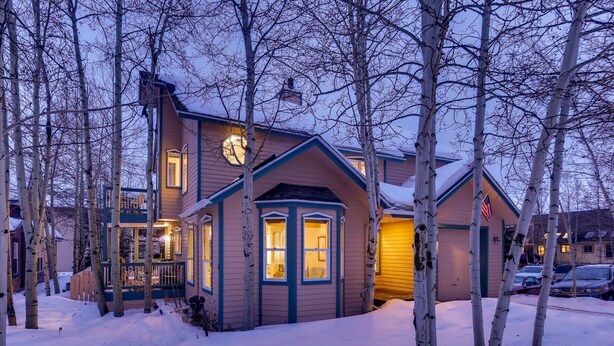 Une maison à deux étages, dotée d’un porche avant imposant, entourée d’arbres couverts de neige.
