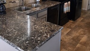 Eine Küche mit Granitarbeitsplatten, einer Edelstahl-Spüle, einem schwarzen Kühlschrank und beigefarbenen Schränken.
