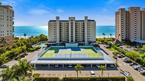 A hotel with a tennis court, parking, and a view of the beach and ocean.