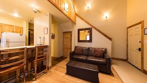 A cozy living area with a wooden dining table, chairs, a leather sofa, and a wooden staircase. - Emmons Condo | 2 Bedroom plus Loft | Steps to Lifts | Shared Hot Tub | Parking (Mt. Crested Butte)