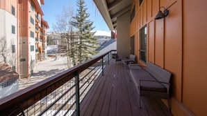 A wooden balcony with a metal railing, a bench, and a wall-mounted light fixture. - Emmons Condo | 2 Bedroom plus Loft | Steps to Lifts | Shared Hot Tub | Parking (Mt. Crested Butte)