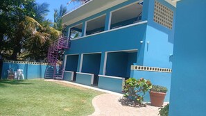 Un bâtiment à deux étages, à la façade bleue, doté d’un escalier en colimaçon et d’un petit jardin agrémenté de plantes en pot.