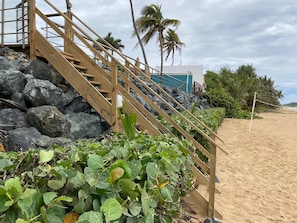 A wooden staircase leading to a building with a view of the beach and palm trees.