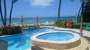 A pool with a view of the ocean, surrounded by palm trees and chairs.