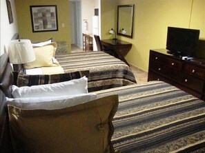 Une chambre d’hôtel avec deux lits, un bureau, une chaise, une télévision et une commode.