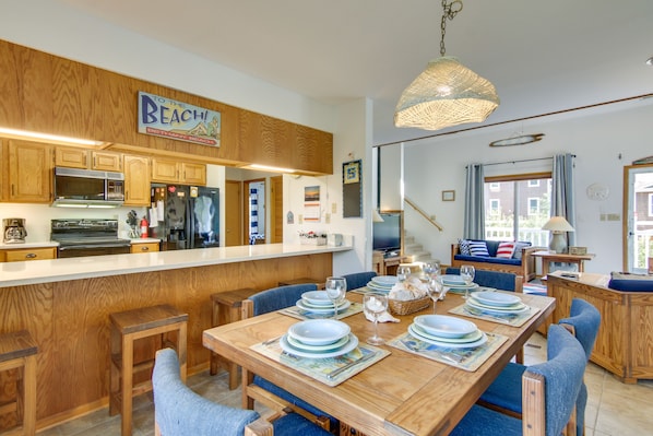 Una cocina con armarios de madera, una isla central y una zona de comedor con sillas azules y una mesa dispuesta para seis personas.
