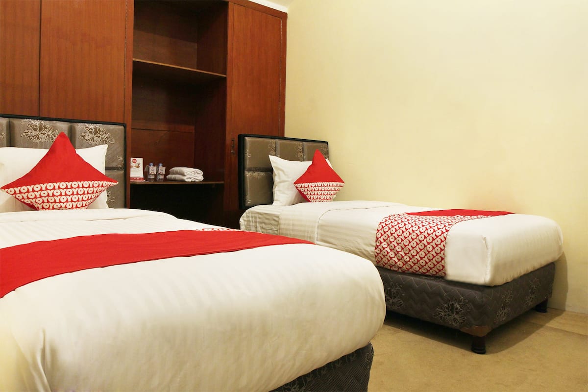 Two beds with red and white bedding, a wooden wardrobe, and a beige carpet.