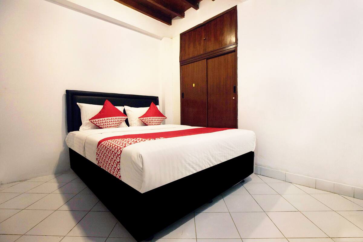 A neatly made bed with a black frame and white bedding, including red and white pillows.
