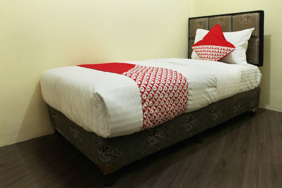 A bed with a patterned bedspread, a red pillow, and a headboard with a floral design.
