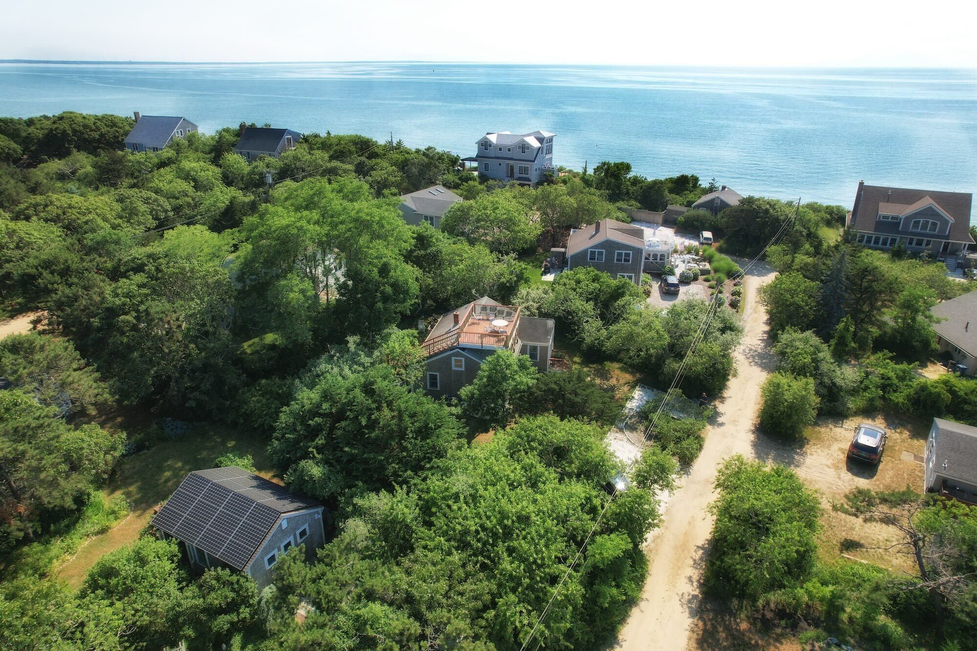 Vista aérea de um bairro residencial com casas cercadas por vegetação densa e uma visão clara do oceano.