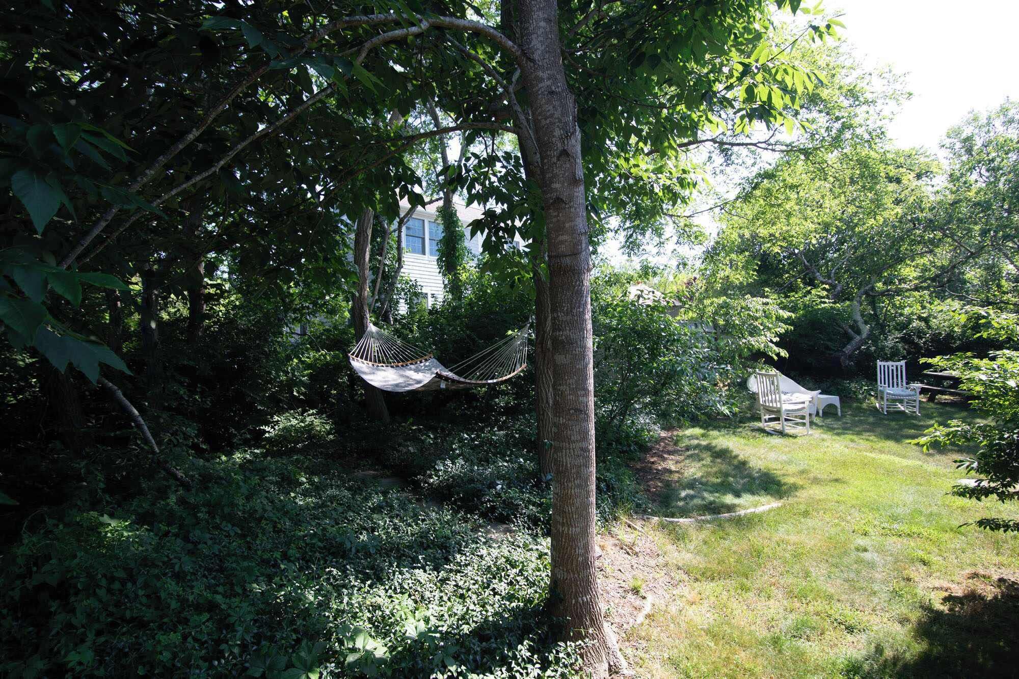 Un hamac est suspendu à un arbre dans un jardin luxuriant, avec un bâtiment blanc en arrière-plan.