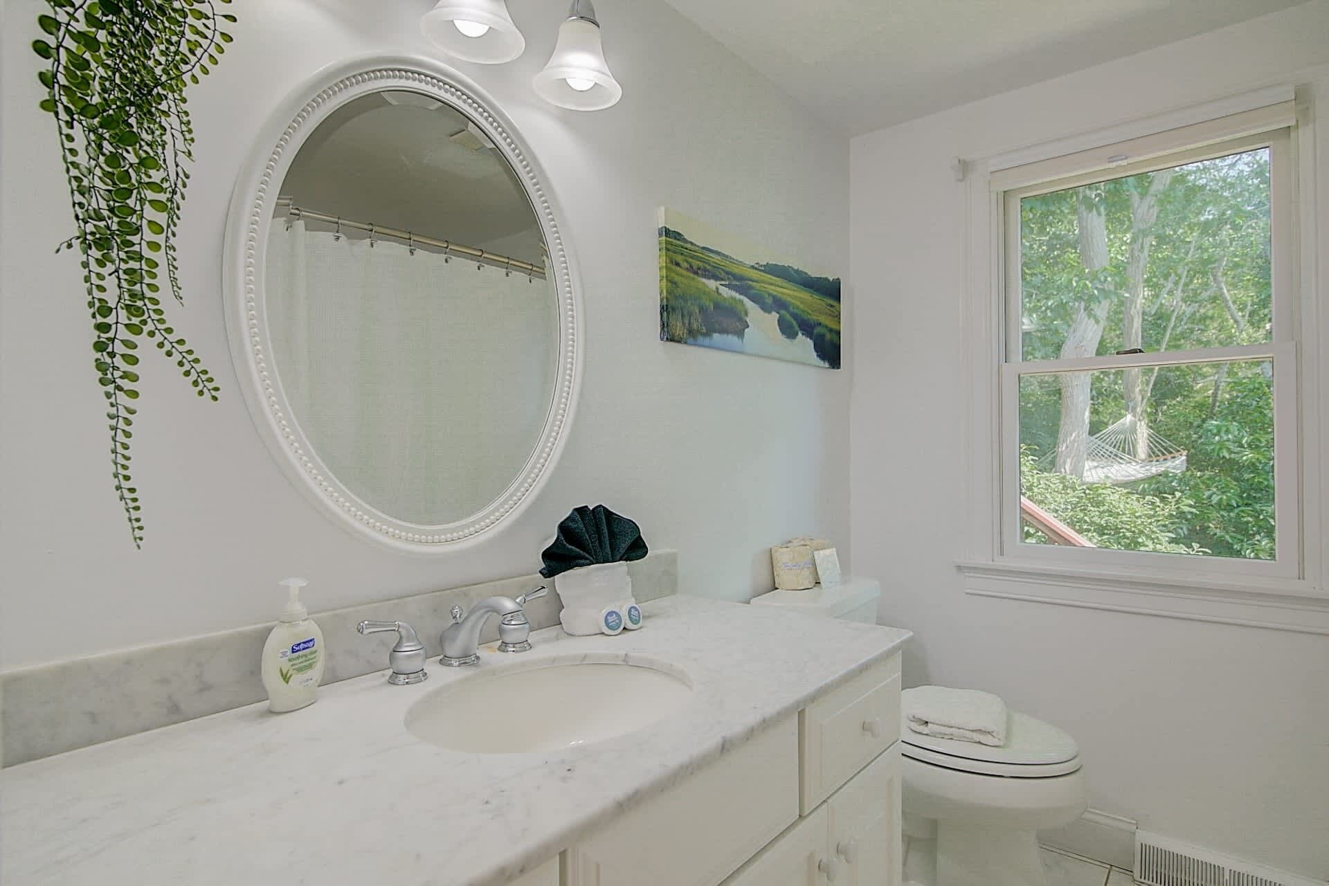 A bathroom with a white sink, mirror, and window.