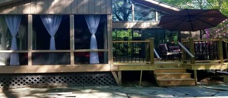 A wooden house with large windows, a deck, and a staircase leading to a covered area with outdoor furniture.