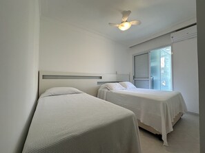 A bedroom with two single beds, a ceiling fan, and a window with blinds.