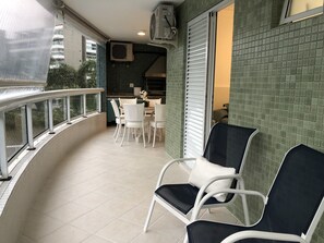 A balcony with white chairs, a table, and a view of a building.