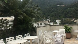 An outdoor patio with white plastic furniture, a potted plant, and a view of a mountain.