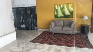 A living room with a beige sofa, a patterned rug, a painting of sailboats, and a marble wall.
