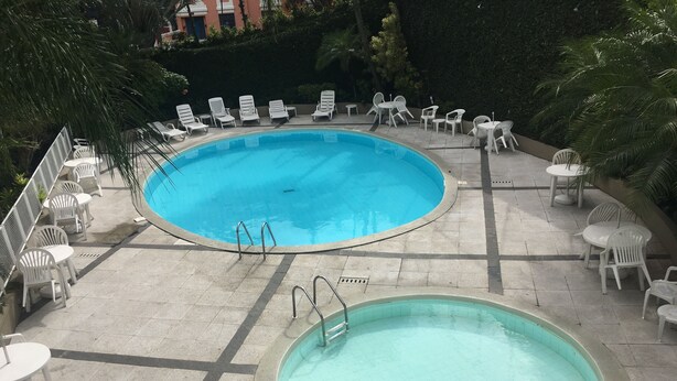 A swimming pool with two separate sections, surrounded by white lounge chairs and tables, and a tiled deck.