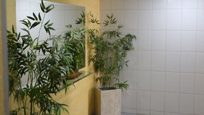 Une salle de bain avec un mur jaune, un miroir et trois plantes en pot.