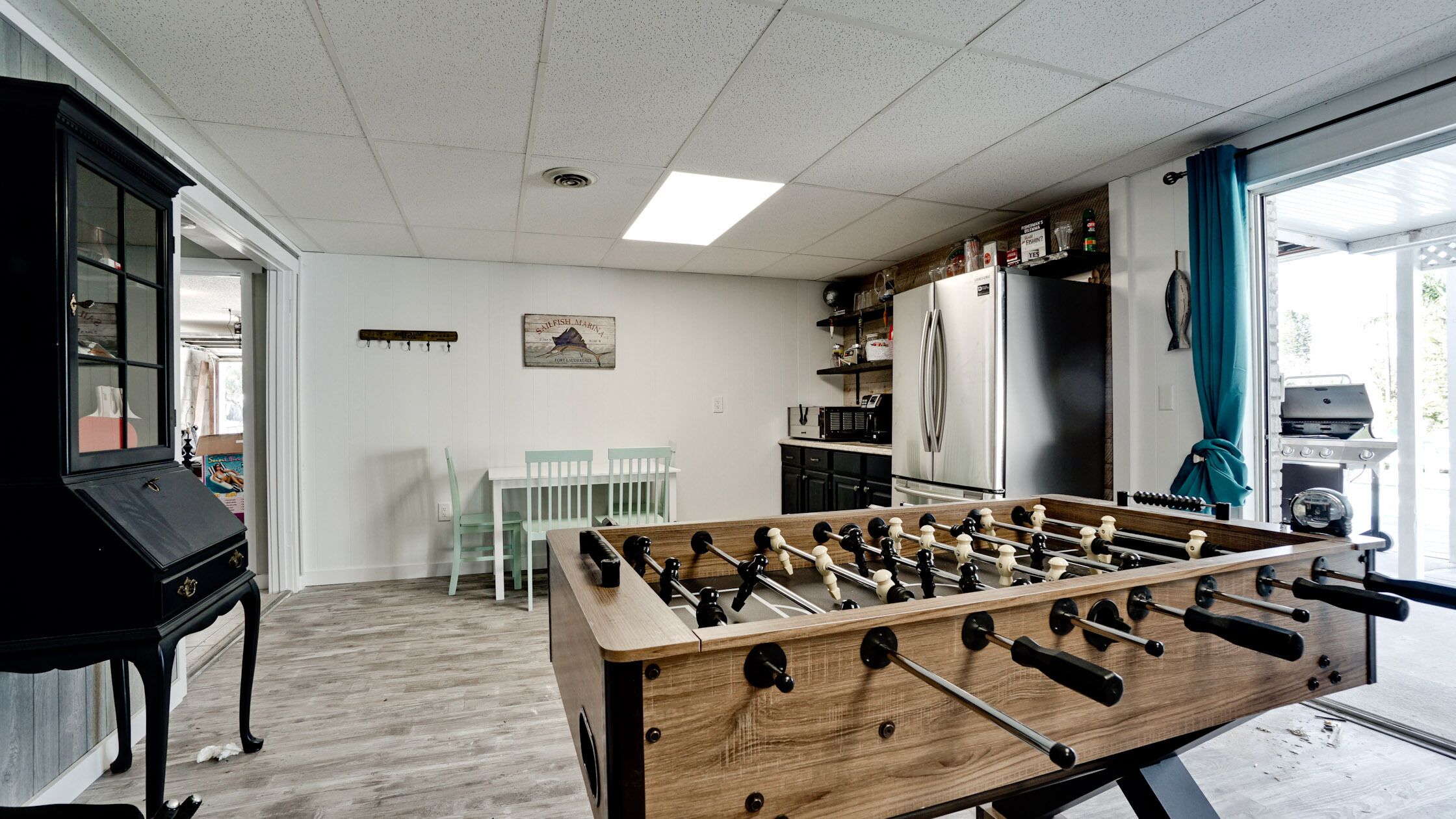 Une pièce comprenant une table de baby-foot, un coin cuisine et une table à manger avec des chaises.
