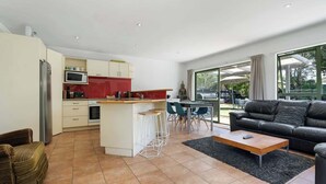 Une cuisine moderne avec des meubles blancs, un mur d’accent rouge et un coin repas comprenant une table et des chaises.