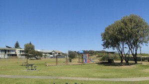 A park with playground equipment, benches, and a large tree. - Sunset on Birubi, 2/40 Ocean Ave - pet friendly, air con, water views, WIFI and outdoor spa (Anna Bay)