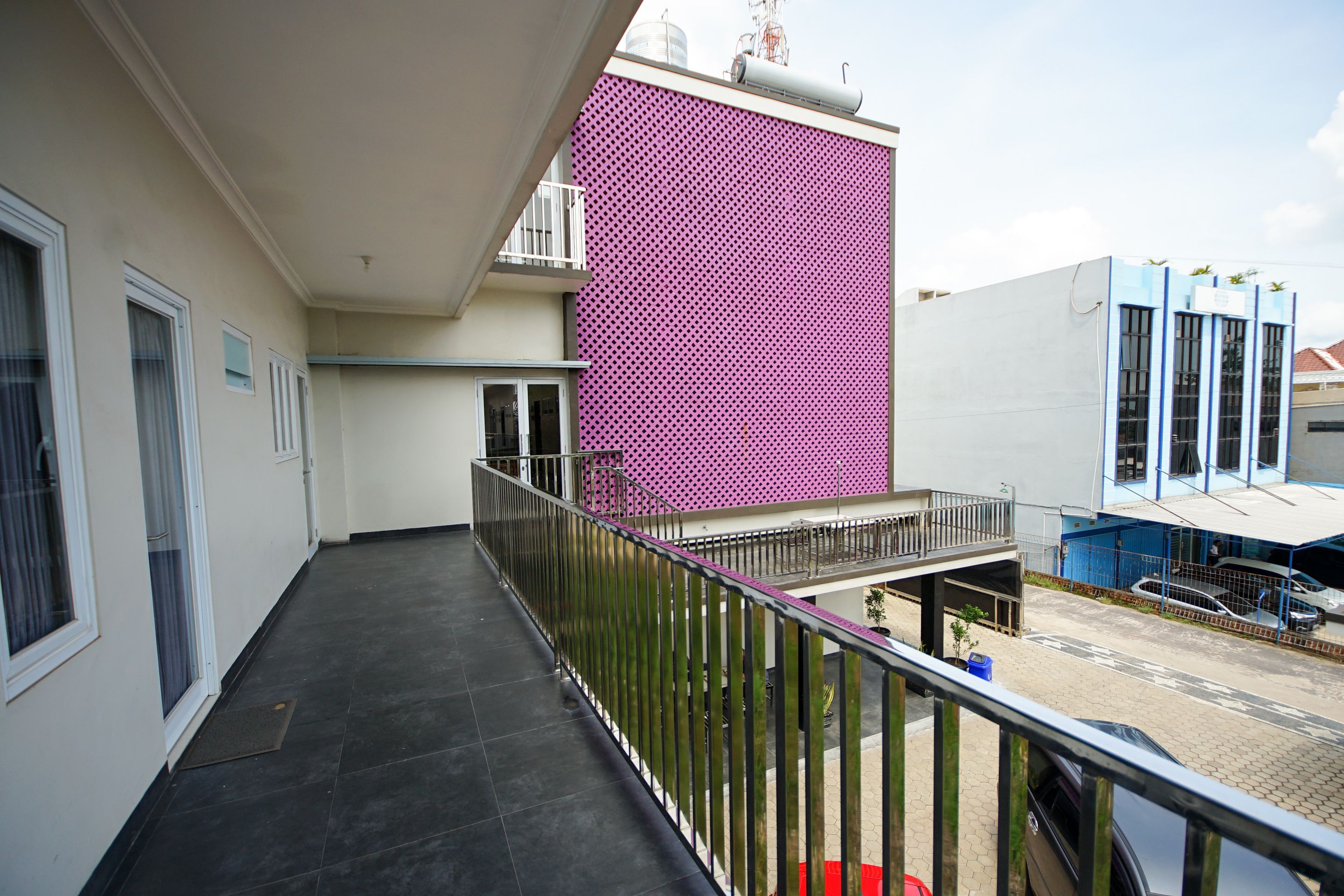 A balcony with a metal railing, a pink perforated wall, and a parking area with cars.