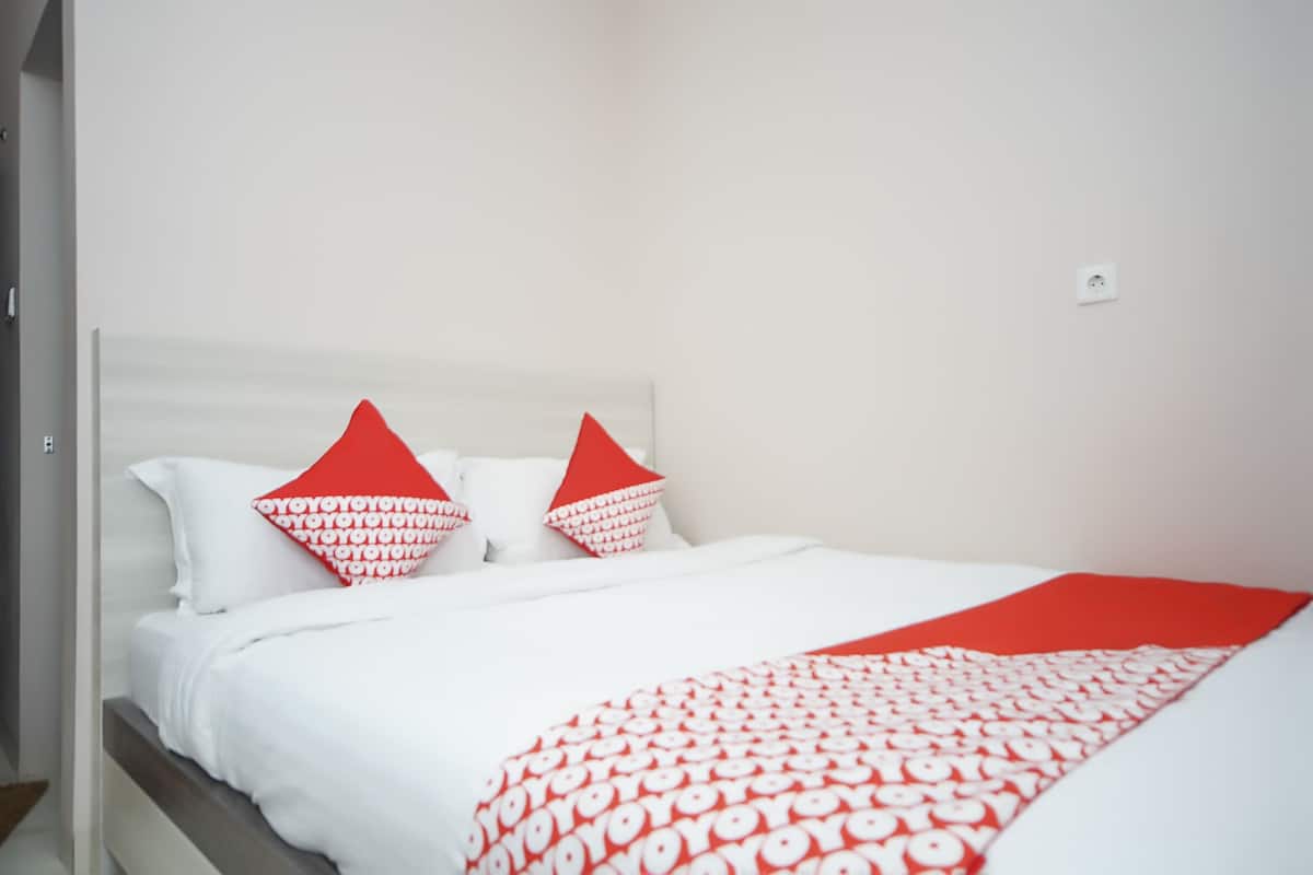 A neatly made bed with white and red bedding, a white headboard, and a red throw blanket.