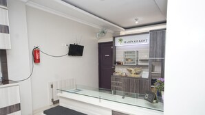 A reception area with a glass counter, a reception desk, a fire extinguisher mounted on the wall, and a sign that reads "MADINAH KOST".