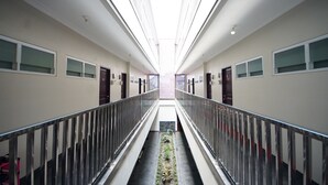 A modern hotel corridor with a central garden, glass railings, and a high ceiling.