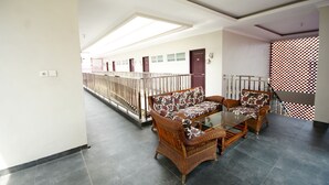 A spacious corridor with a glass table and wicker furniture, leading to a staircase with a patterned railing.