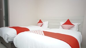 A double bed with white bedding and red accents, including pillows and a throw blanket.