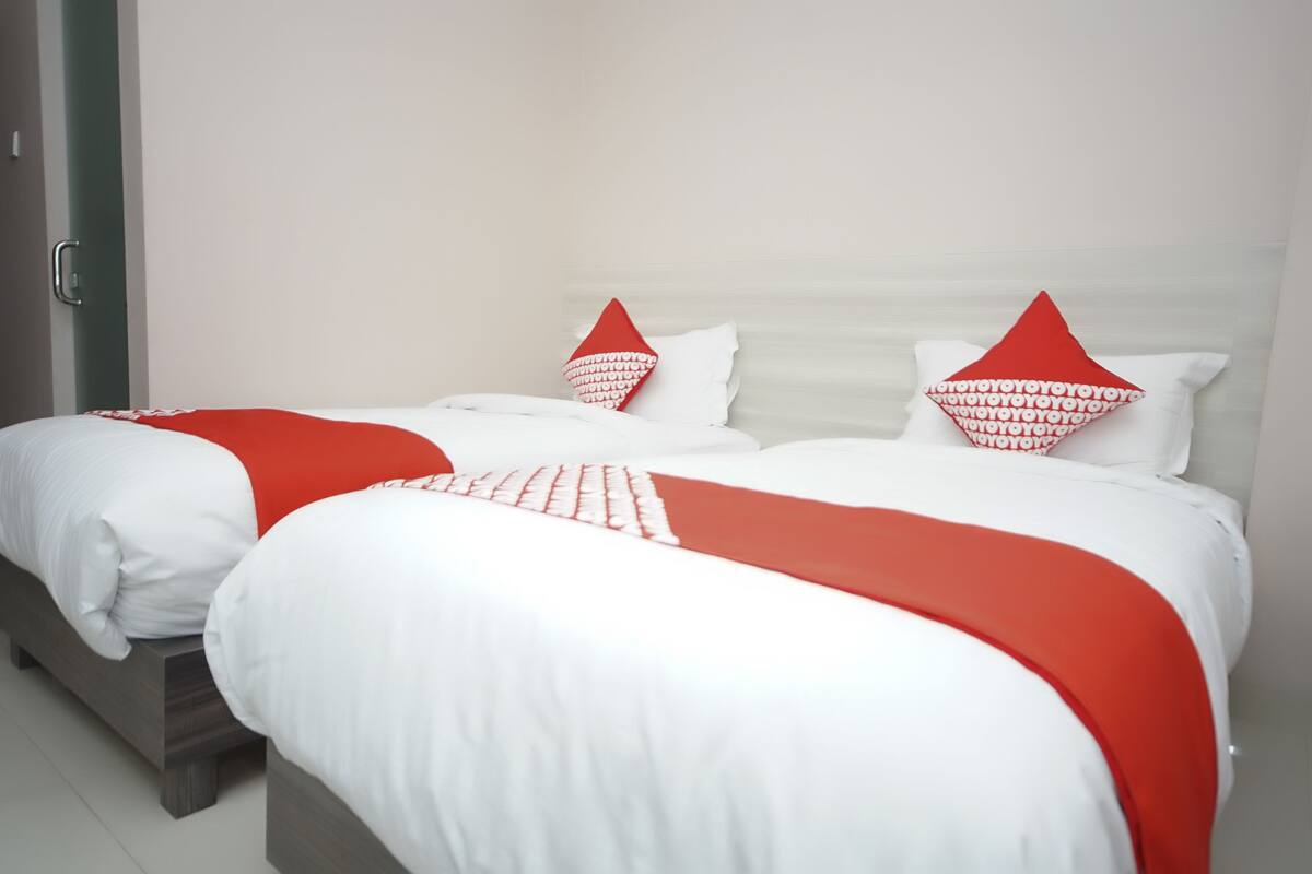 A double bed with white bedding and red accents, including pillows and a throw blanket.