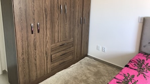 Ein Schlafzimmer mit großem Holzschrank, einem Bett mit rosa geblümter Tagesdecke und Teppichboden.
