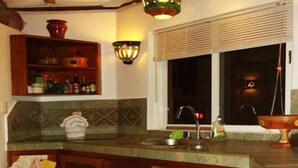 A kitchen with wooden cabinets, a tiled backsplash, and a window with blinds. - The only and most charming luxury beachfront cottage on the Riviera Maya (Akumal)